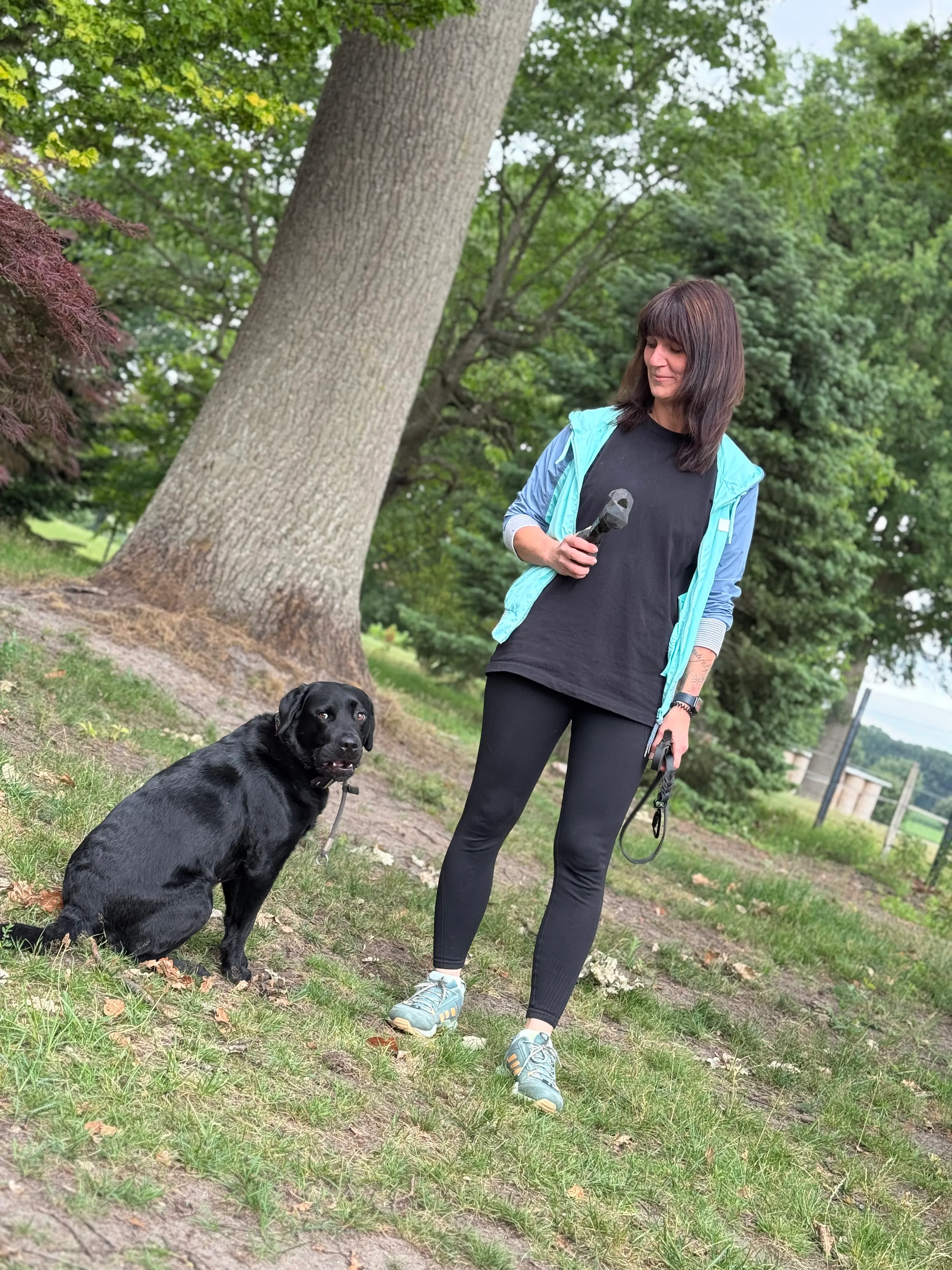Frau steht mit schwarzem Hund auf einer Wiese im Training